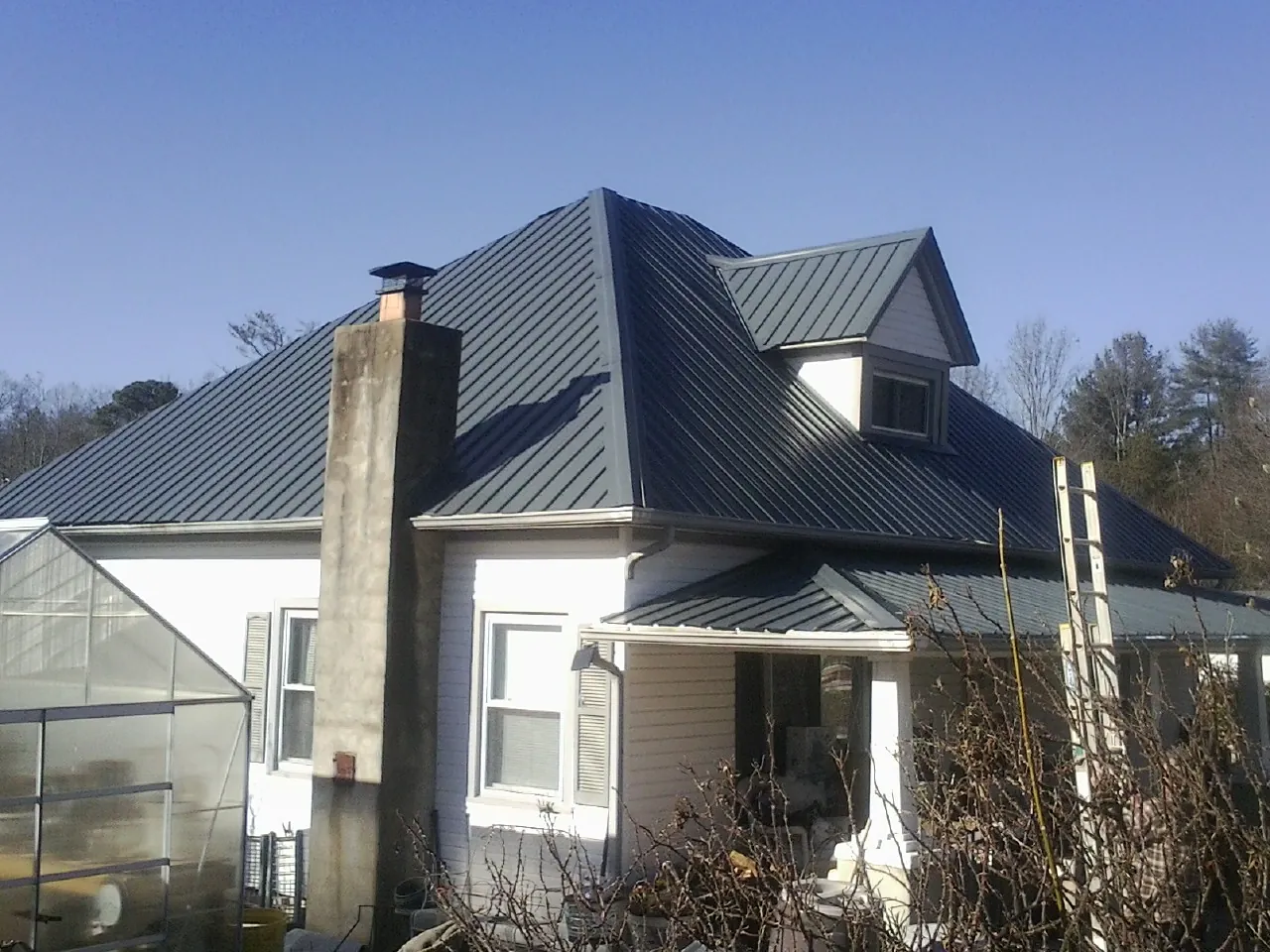 Dark blue standing seam metal roof on a white farmhouse with dormer — Slate & Tile Roof Repair by Roofing Brothers in Pearland