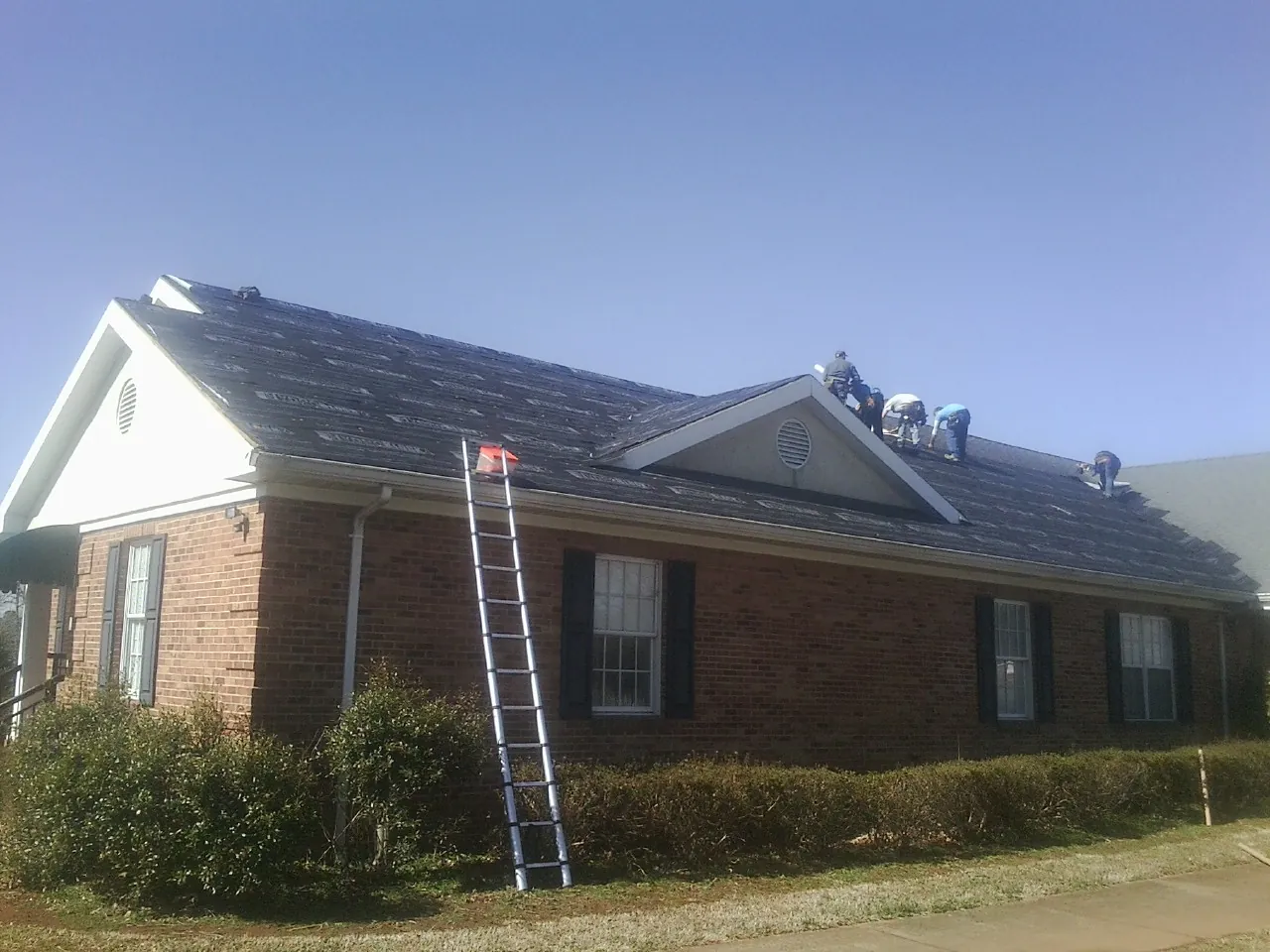 Crew tearing shingles off a brick ranch roof with a ladder set — Emergency Roof Repair work by our crew in Pearland