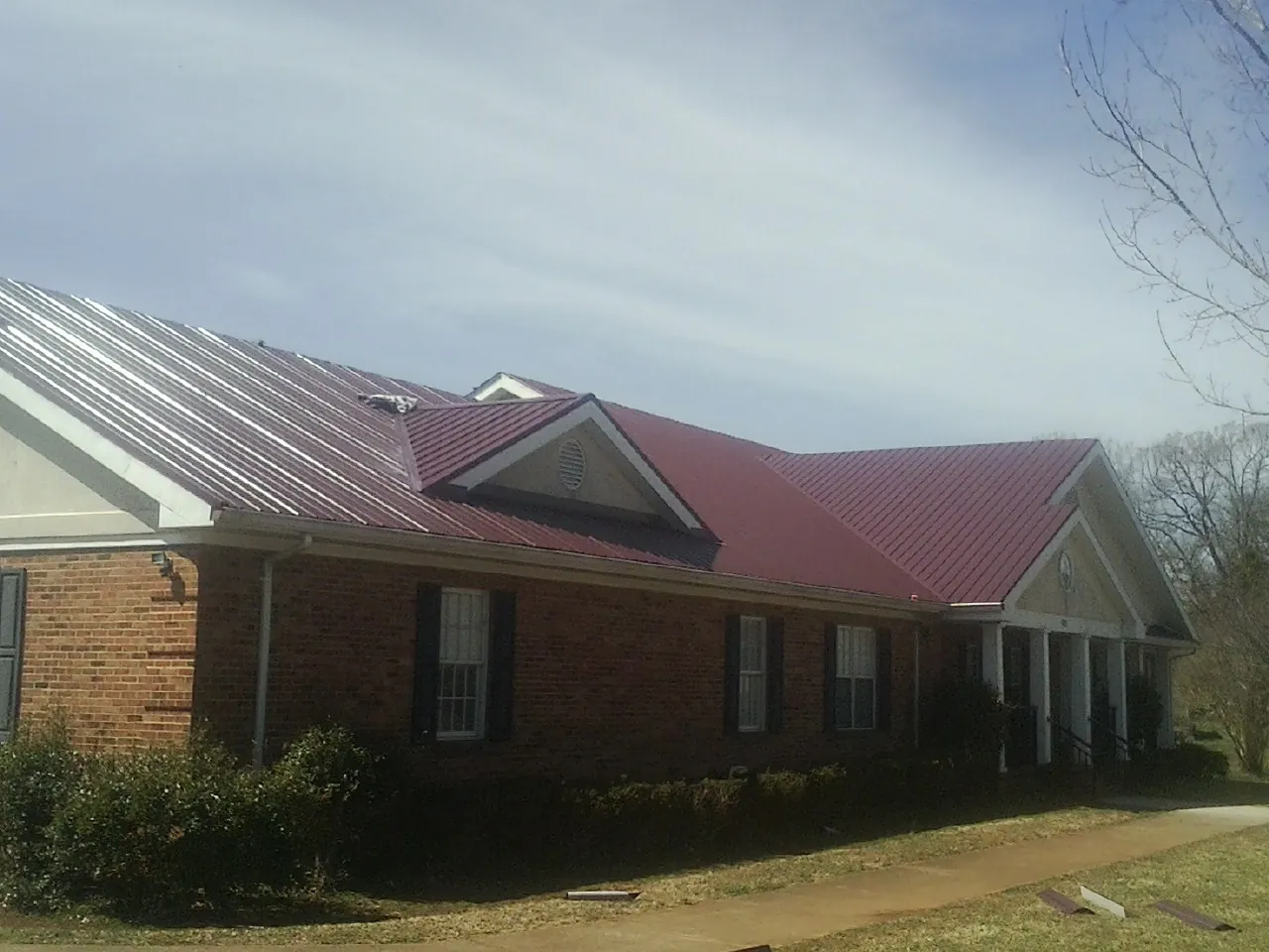 Red metal roof with gabled entries on a long brick building, from a Hail Damage Roof Repair job in Pearland