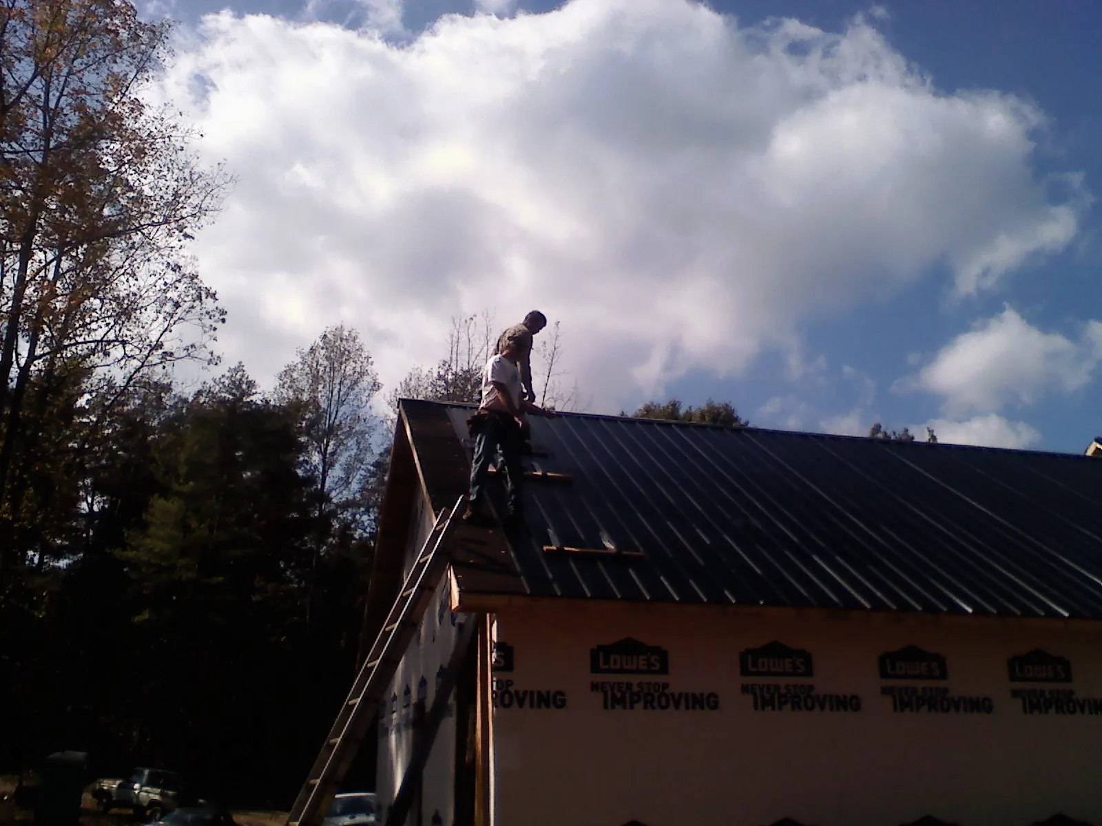 Roofer fastening dark metal panels high against a cloudy sky, from a Roof Inspection job in Pearland