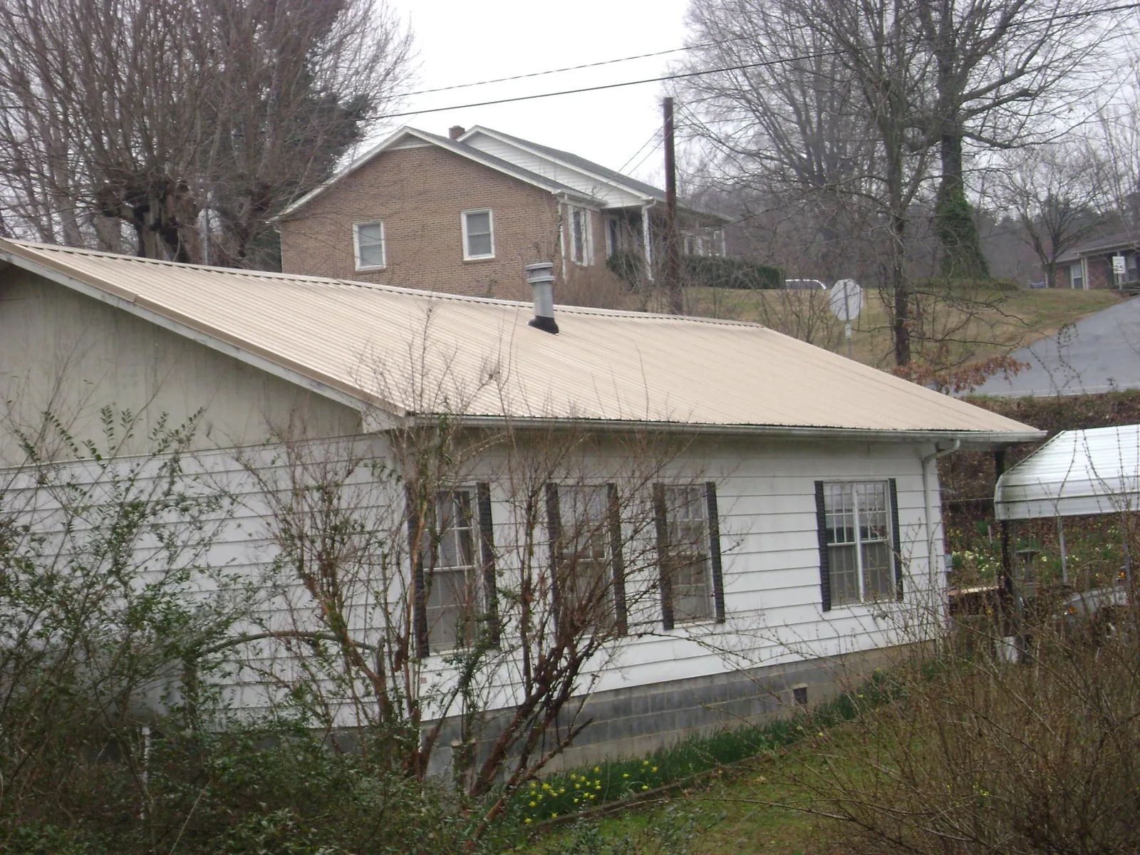 Tan metal roof on a white sided house set into a hillside — Commercial Roofing by Roofing Brothers in Pearland